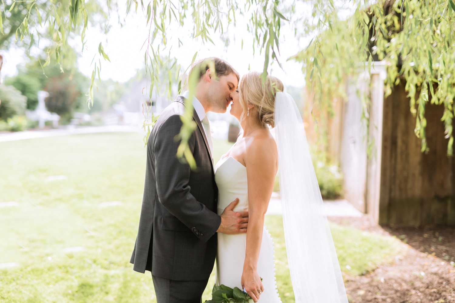 Bride and groom kissing under a willow tree at Amber Grove during summer wedding in Richmond, Virginia