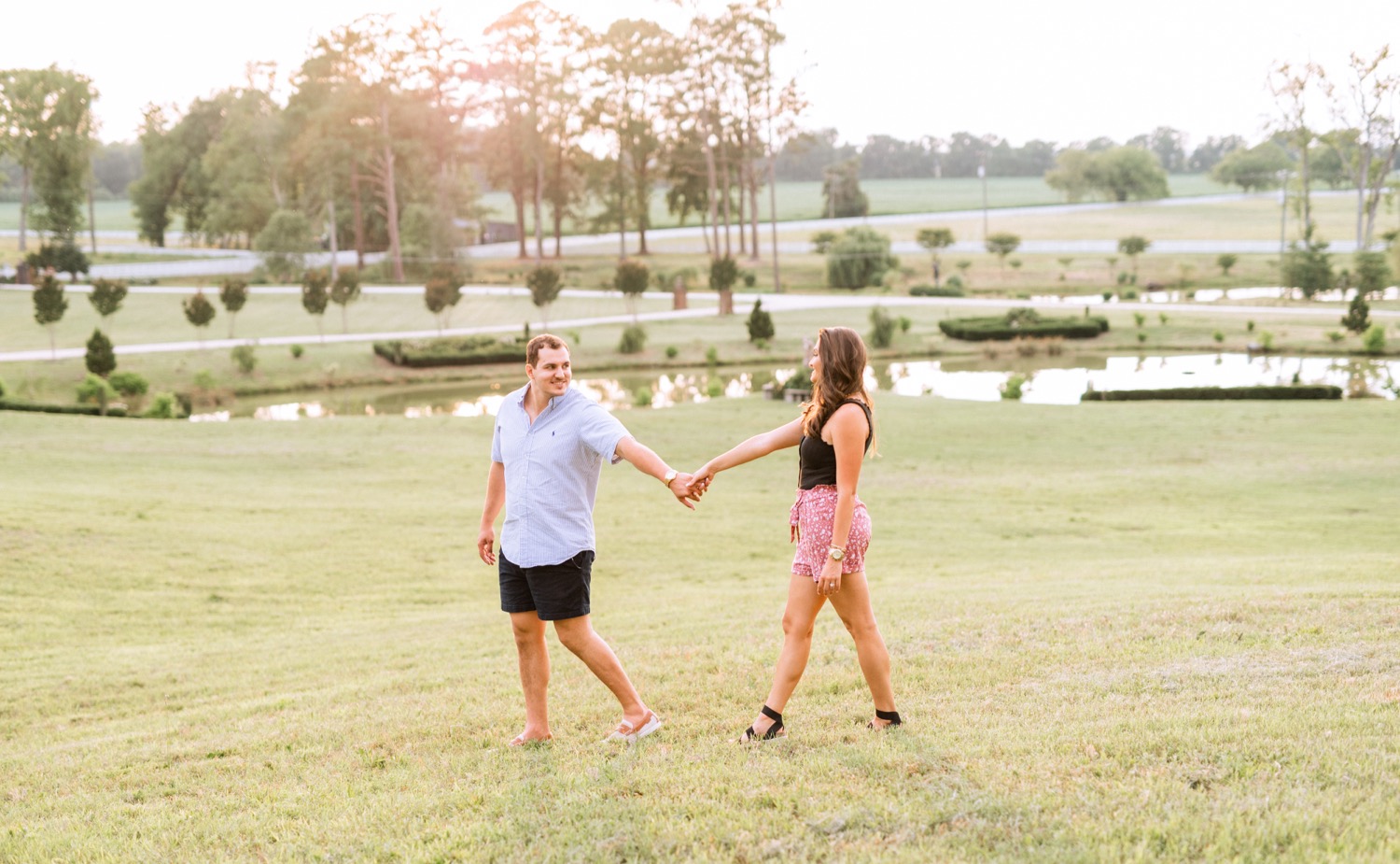 engaged couple holding hands and walking through the field in front of the lake at the cumberland estate in richmond virginia
