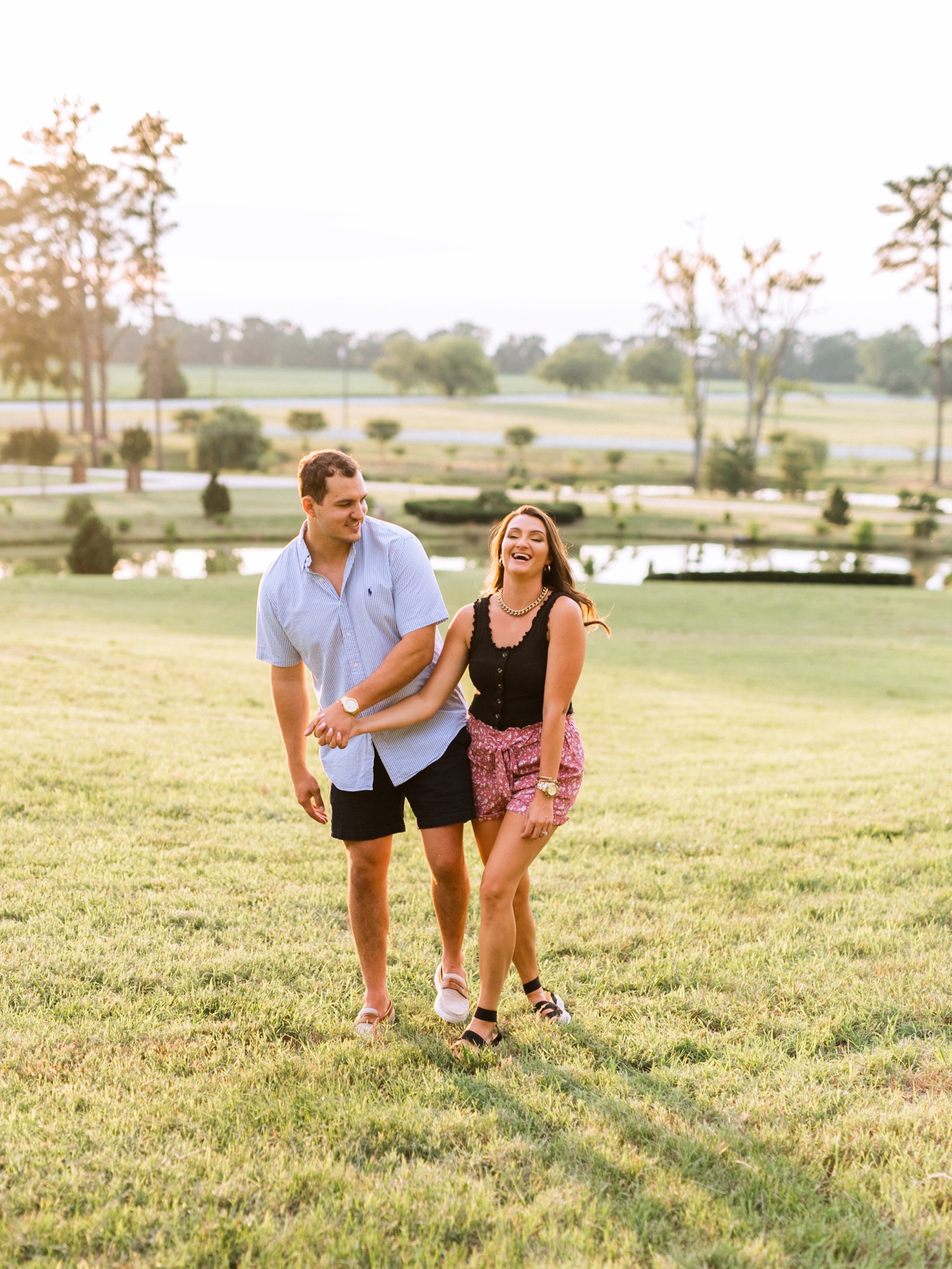 engaged couple holding hands and walking through the field in front of the lake at the cumberland estate in richmond virginia