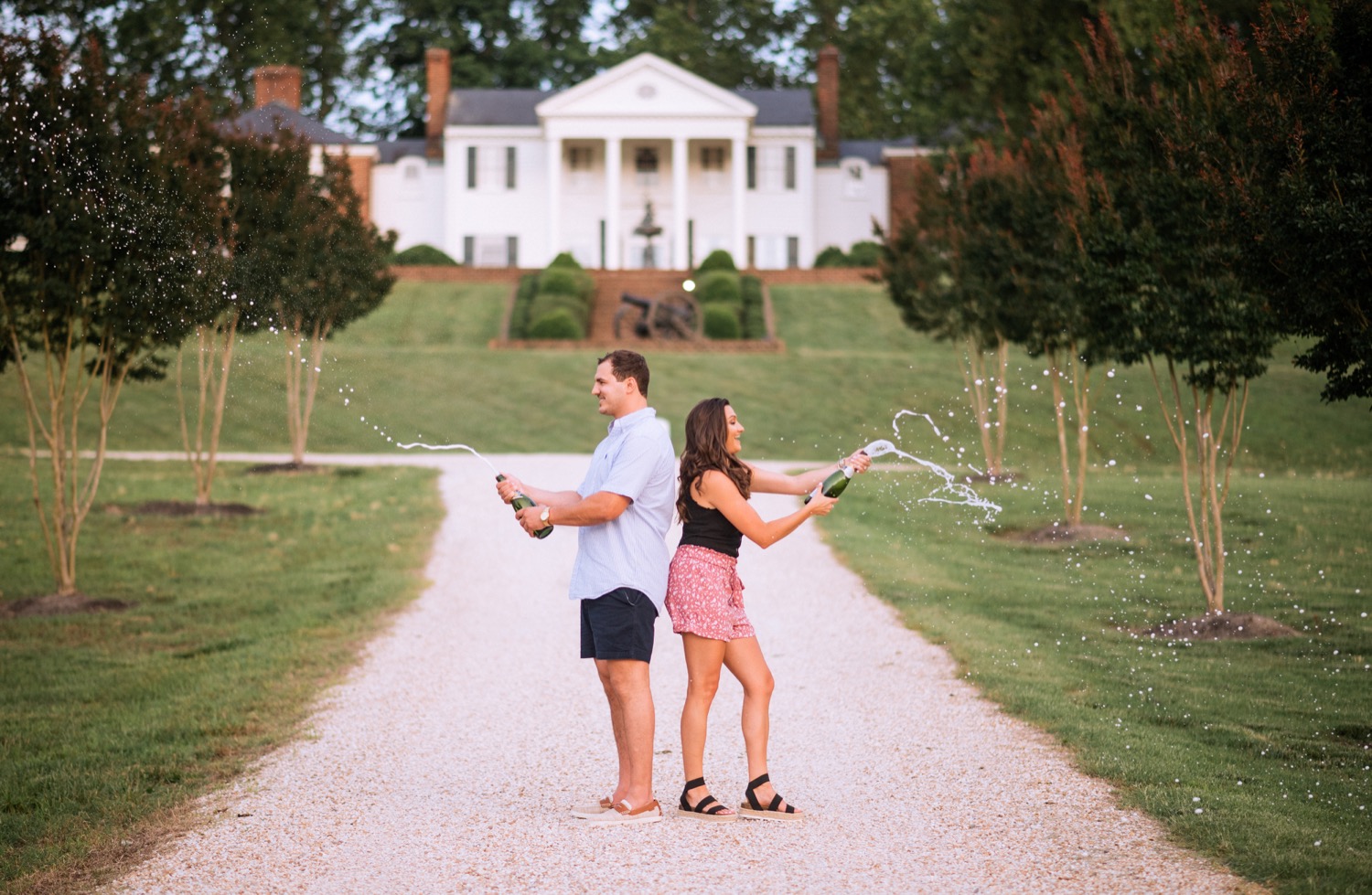 engaged couple popping champagne bottles on driveway that leads up to the cumberland estate in richmond virginia