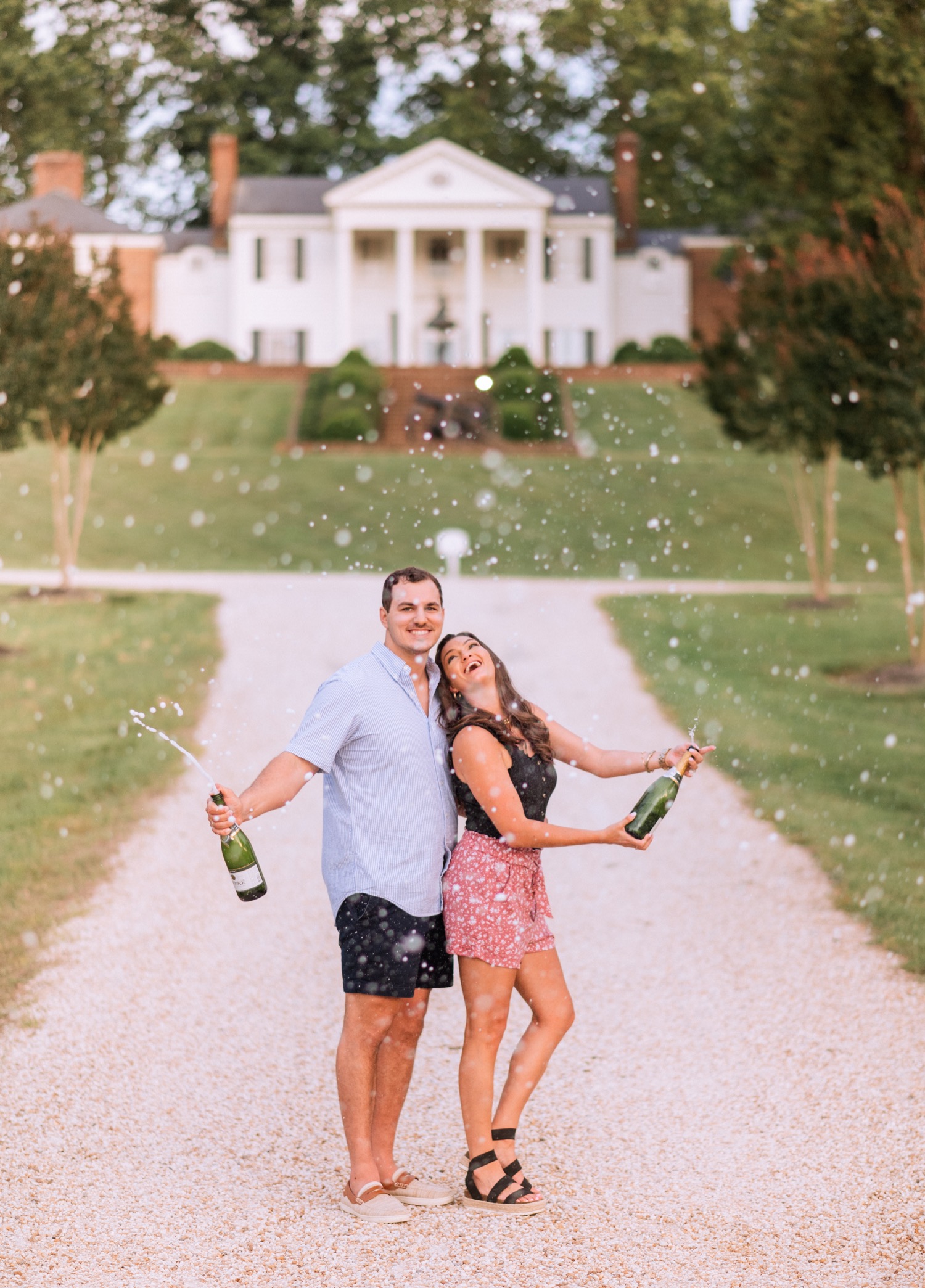 engaged couple popping champagne bottles on driveway that leads up to the cumberland estate in richmond virginia