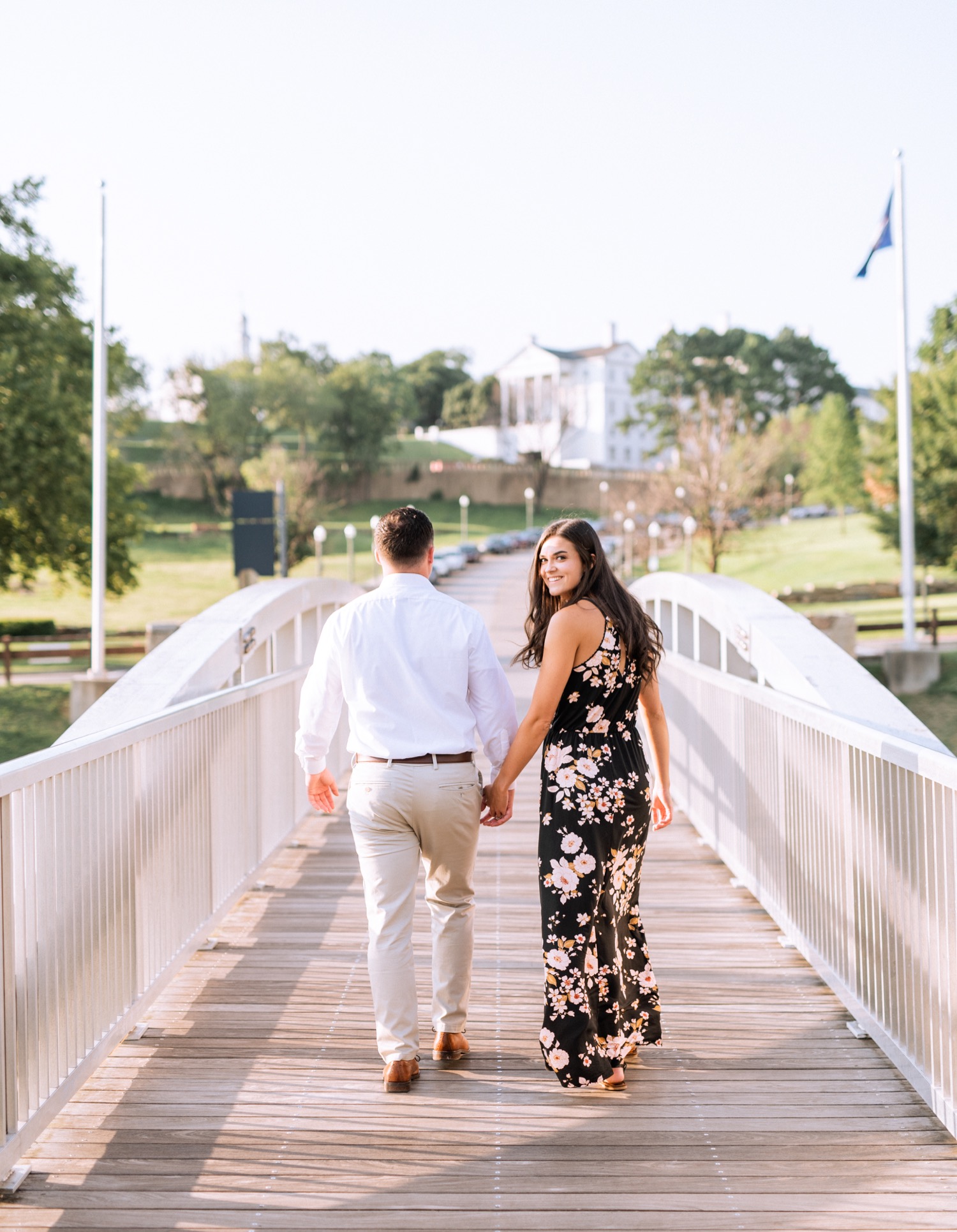 woman in long dress and man in white button down and khakis walking on a bridge