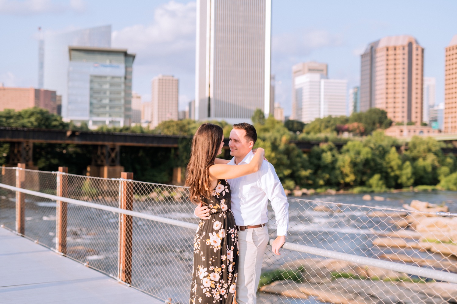 engaged couple hugging and kissing with skyline and river flowing behind them