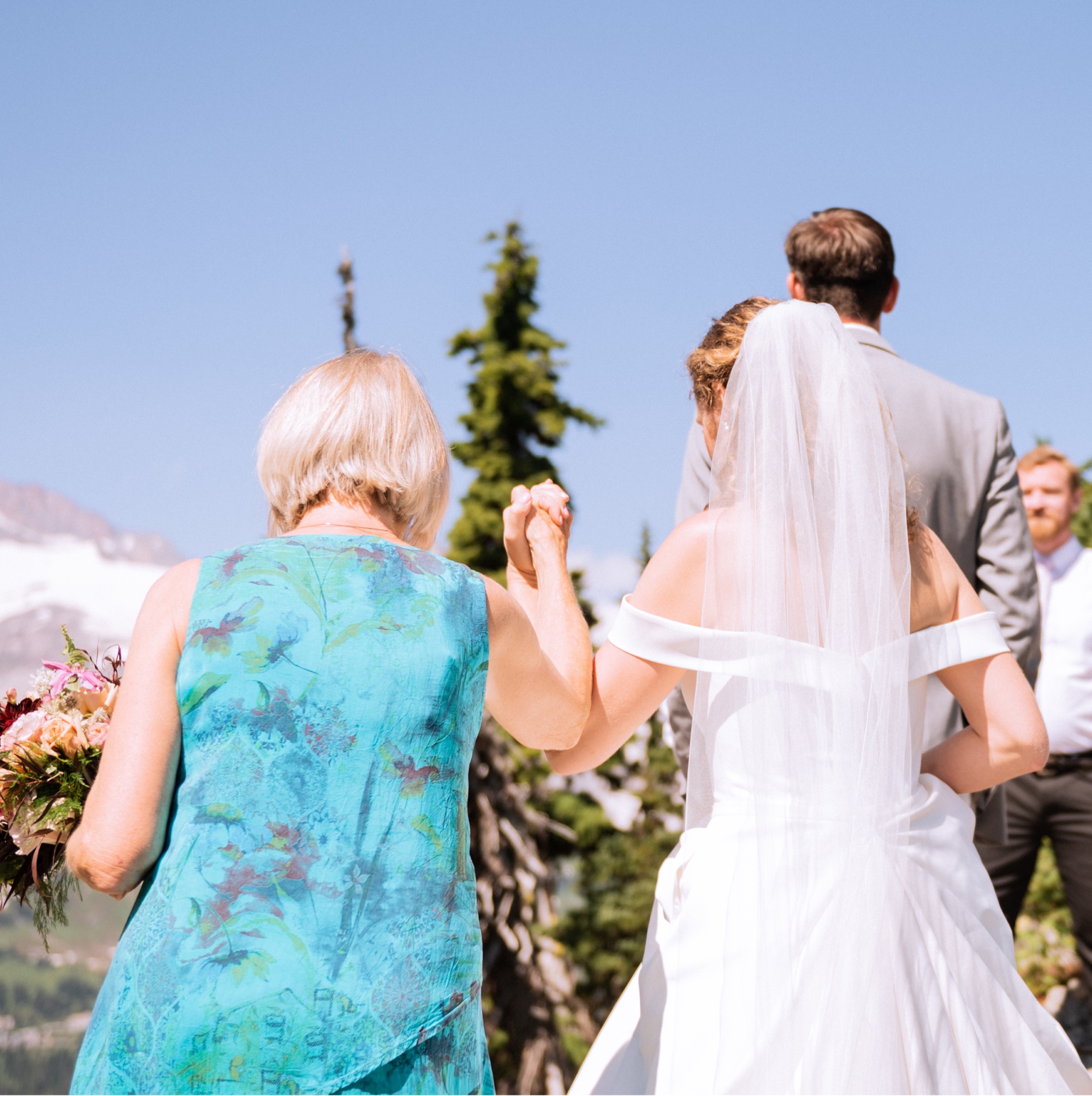 grandma holds the hand of bride as they meet her groom on the alter at the top of mt rainier