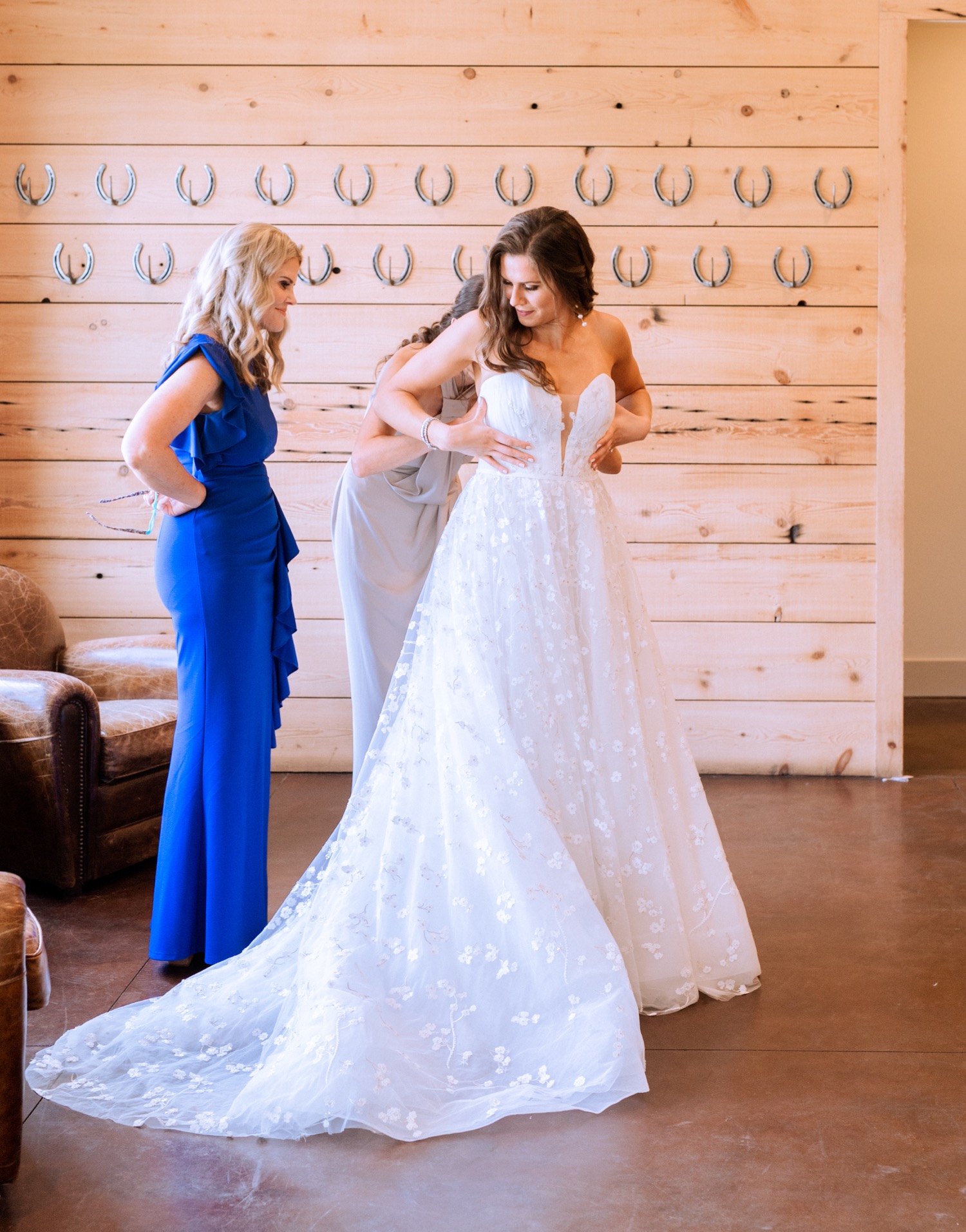 bride with her mom and mother in law zipping up her wedding dress to head to the ceremony