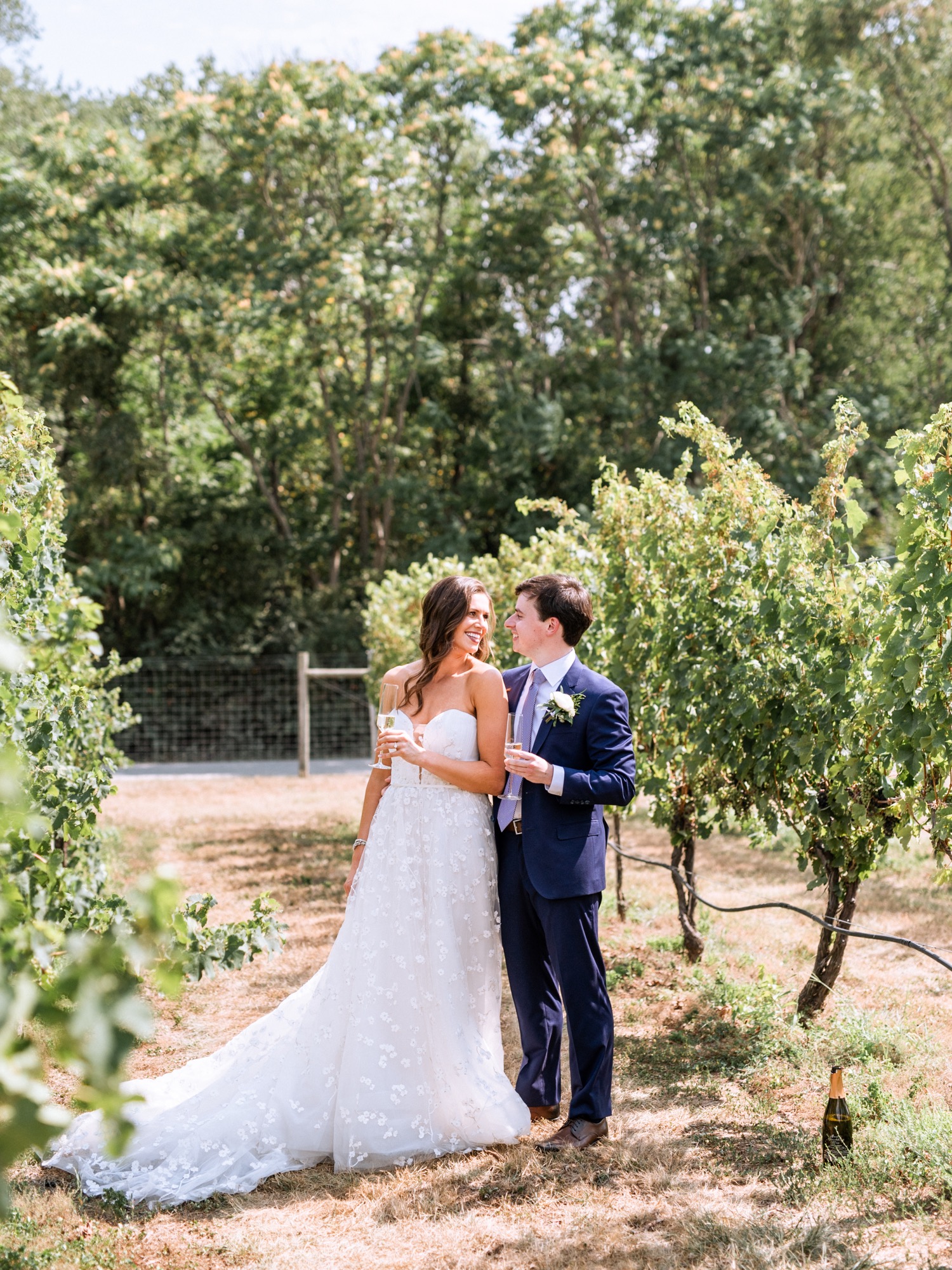 bride and groom walking through the vineyard and sharing a glass of champagne during their Charlottesville wedding day 