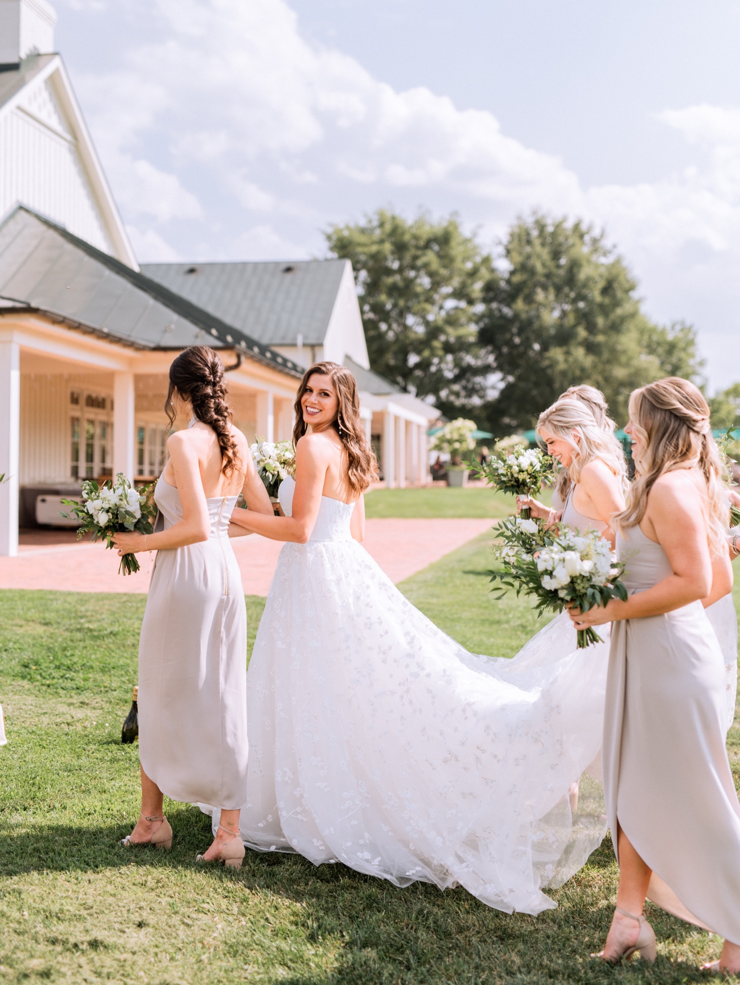 bride walking with her bridesmaids carrying her dress