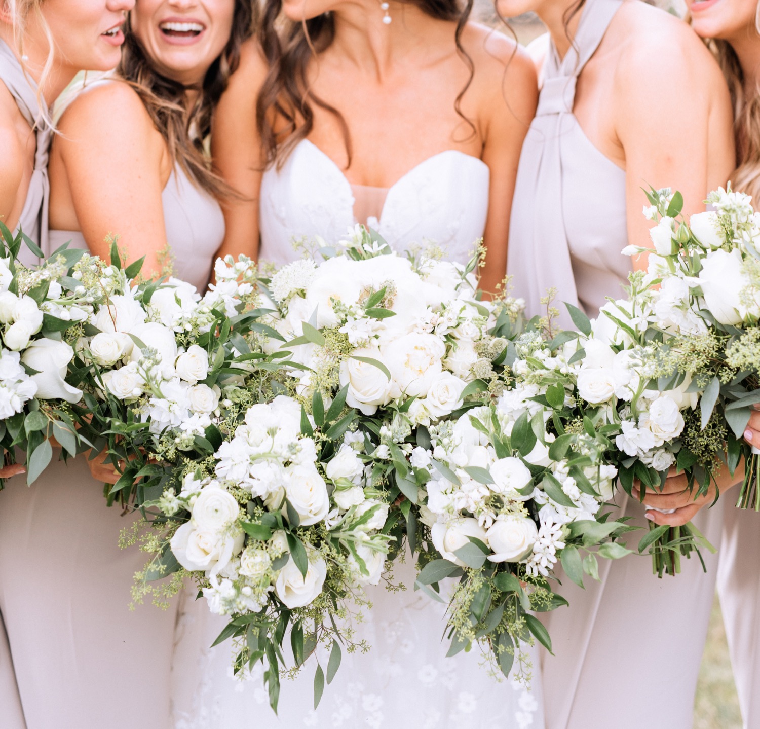 white flower arrangements with the bride and bridesmaids in taupe dresses holding them in front 