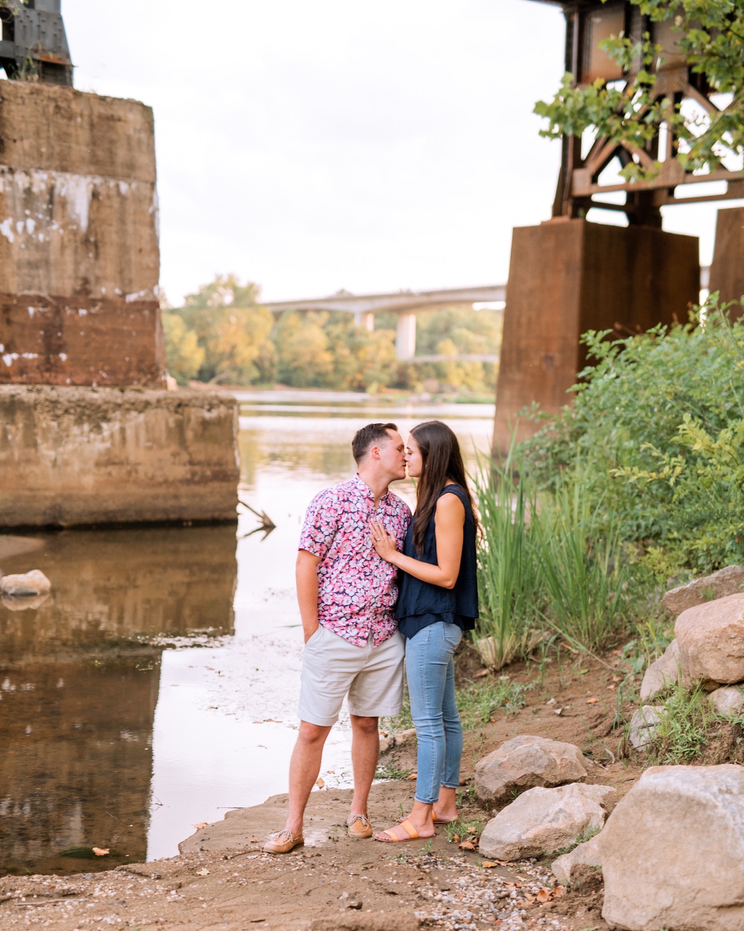 engaged couple hugging and kissing under the bridge along the water in browns island