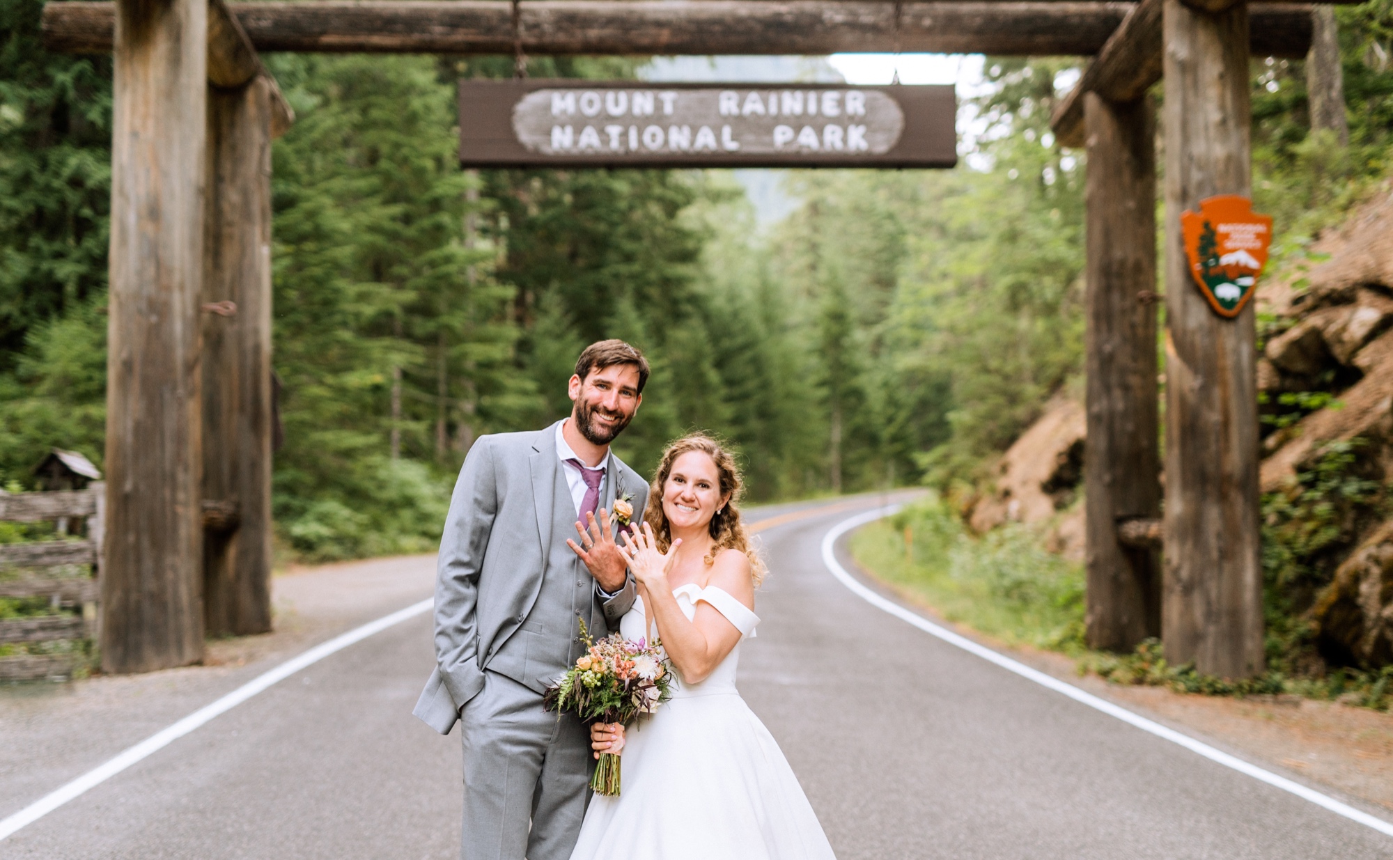 bride and groom standing underneath the entrance sign to mount rainier national park