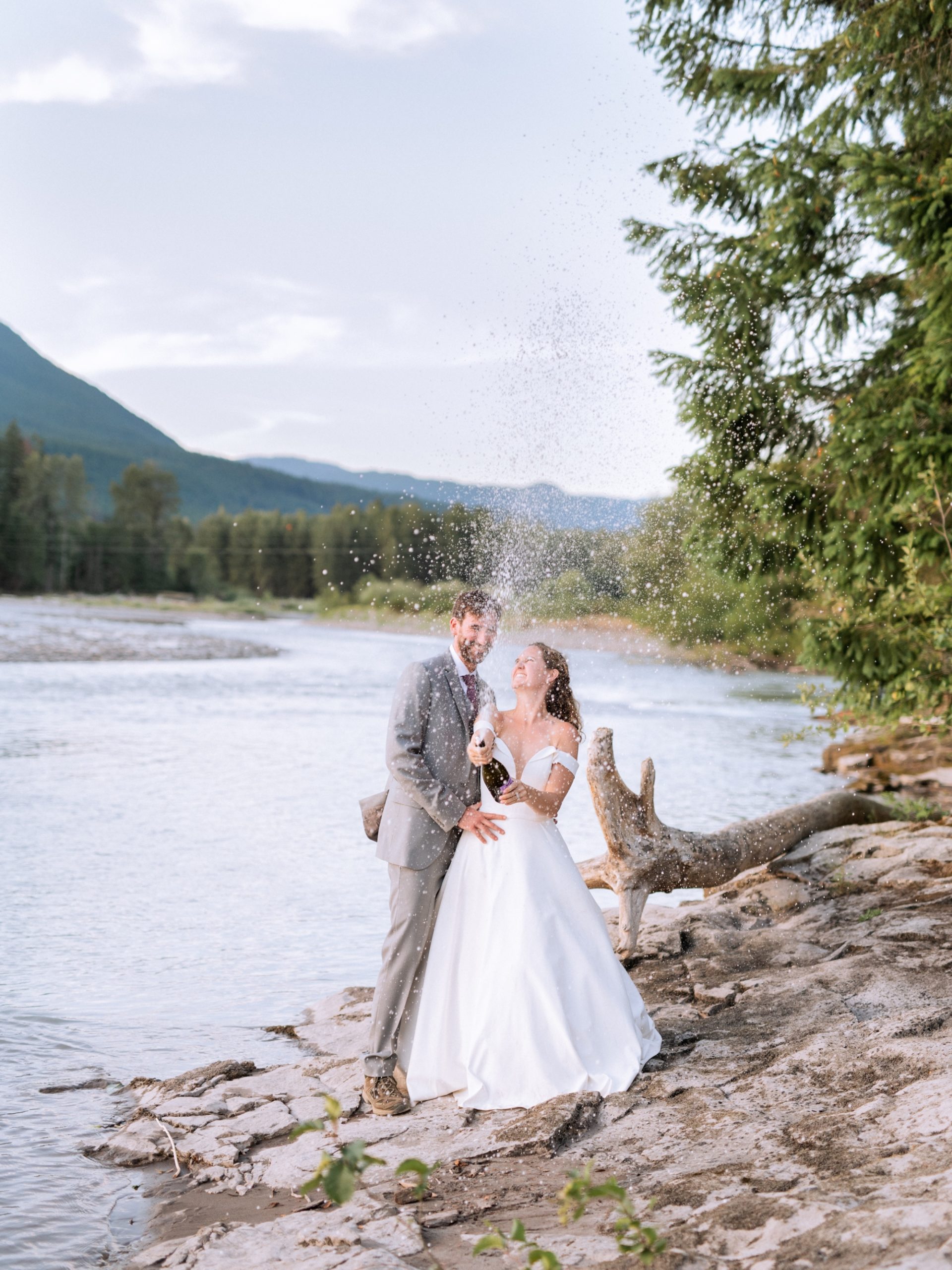 bride and groom pop champagne bottle on riverbank in mt rainier national park