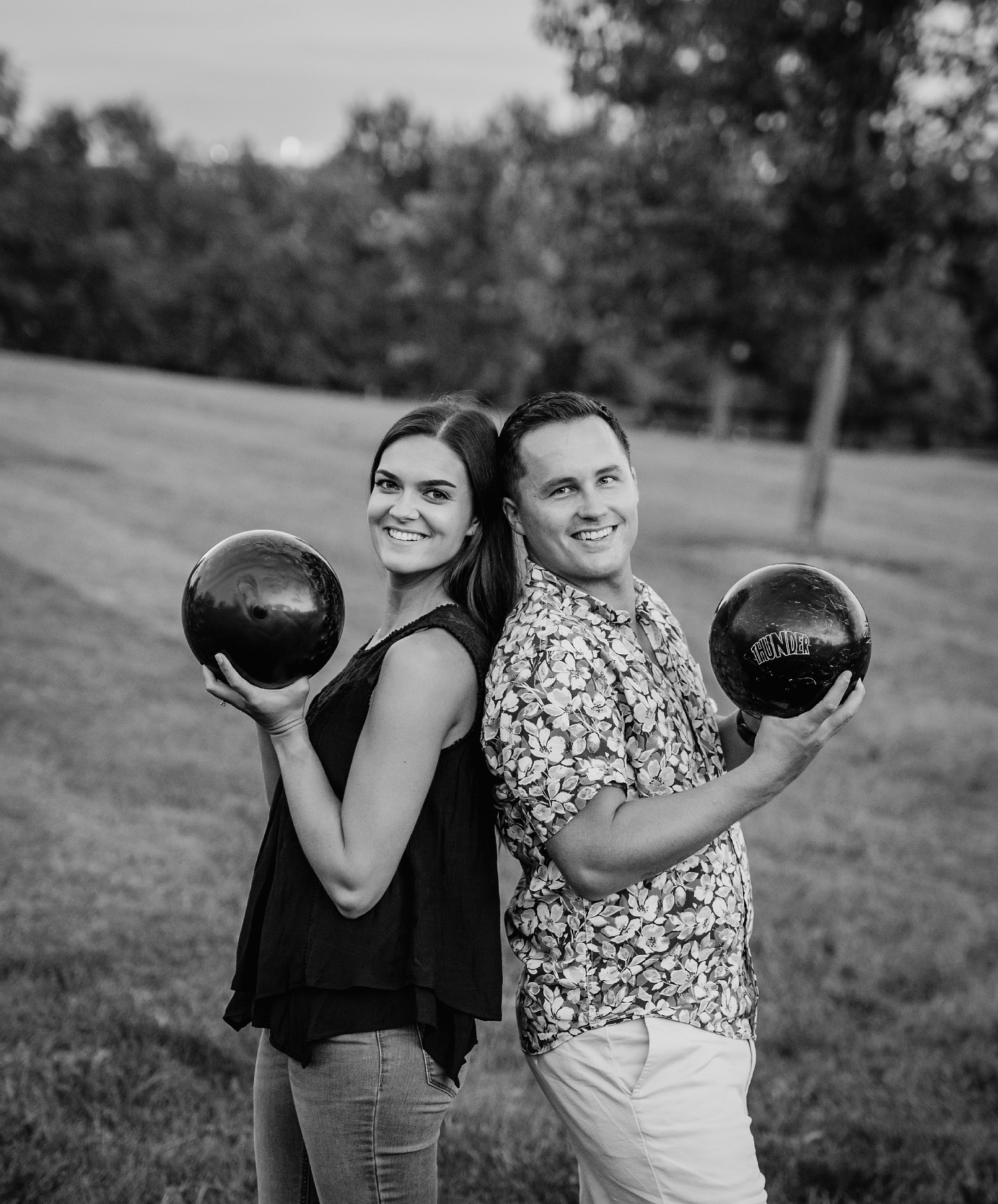 engaged couple standing back to back posing with their personal bowling balls