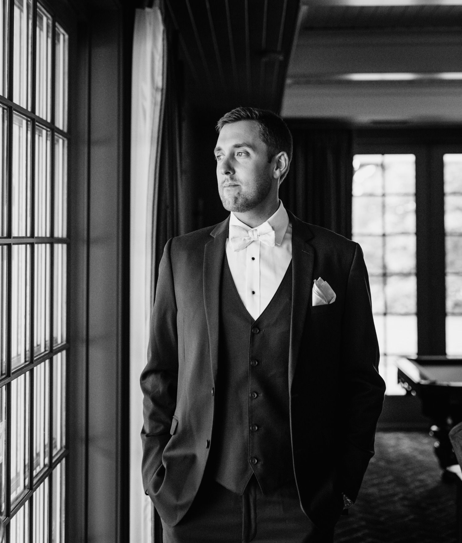 groom in tux staring out the window at the keswick vineyards venue