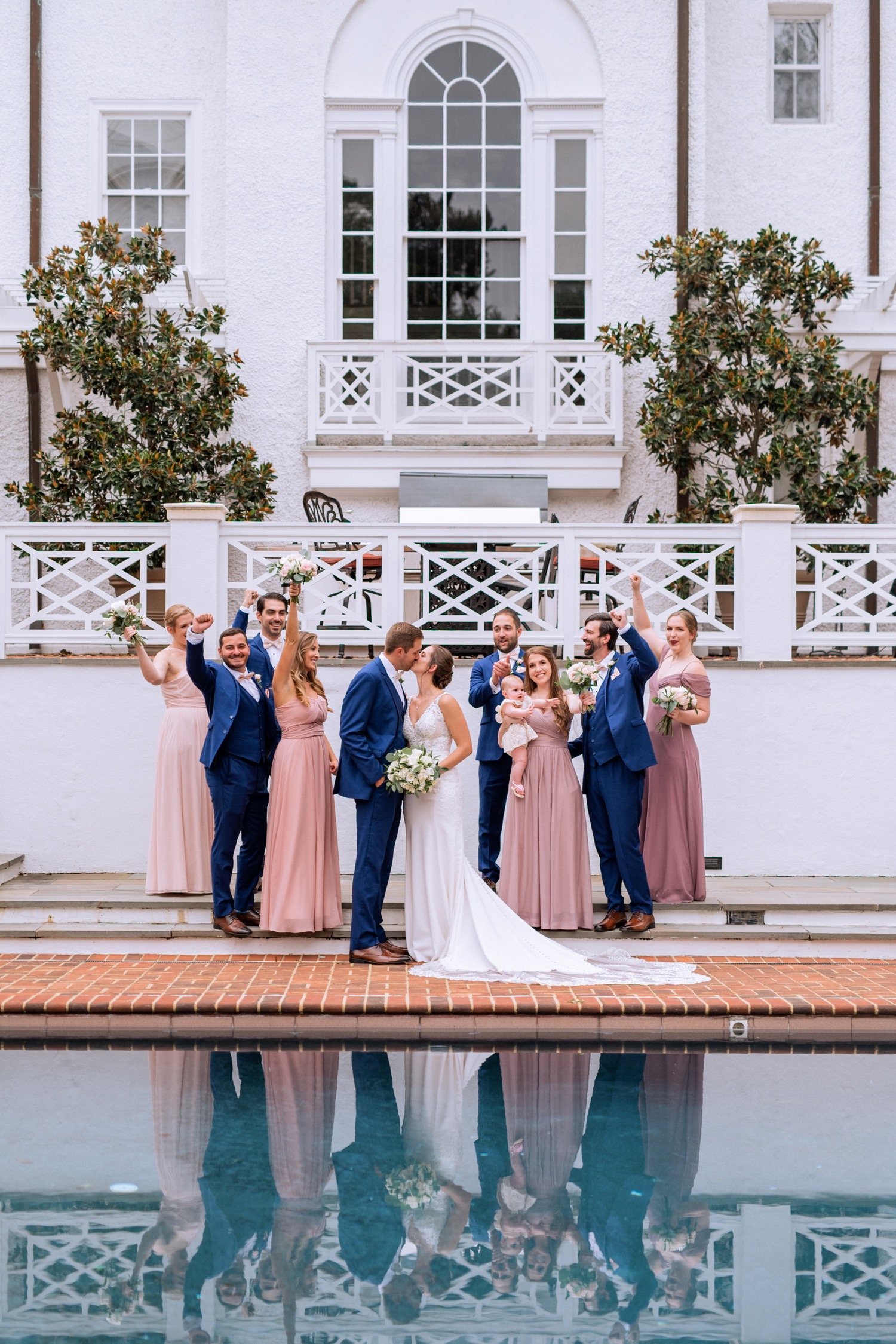 entire wedding party wearing light pink and purple dresses and navy blue tuxes posing and walking with the bride and groom on their wedding day
