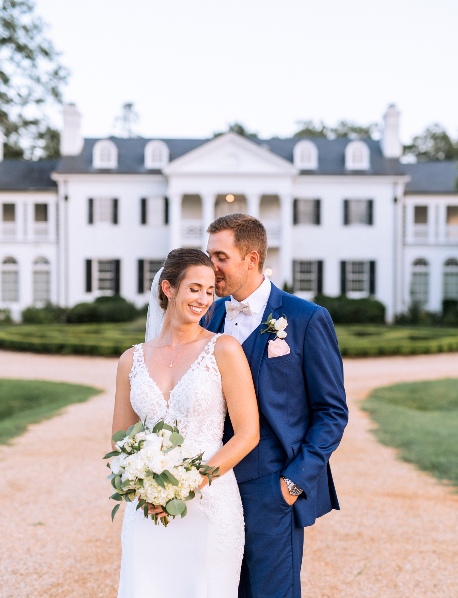 bride and groom holding each other close in front of the white mansion at keswick vineyards
