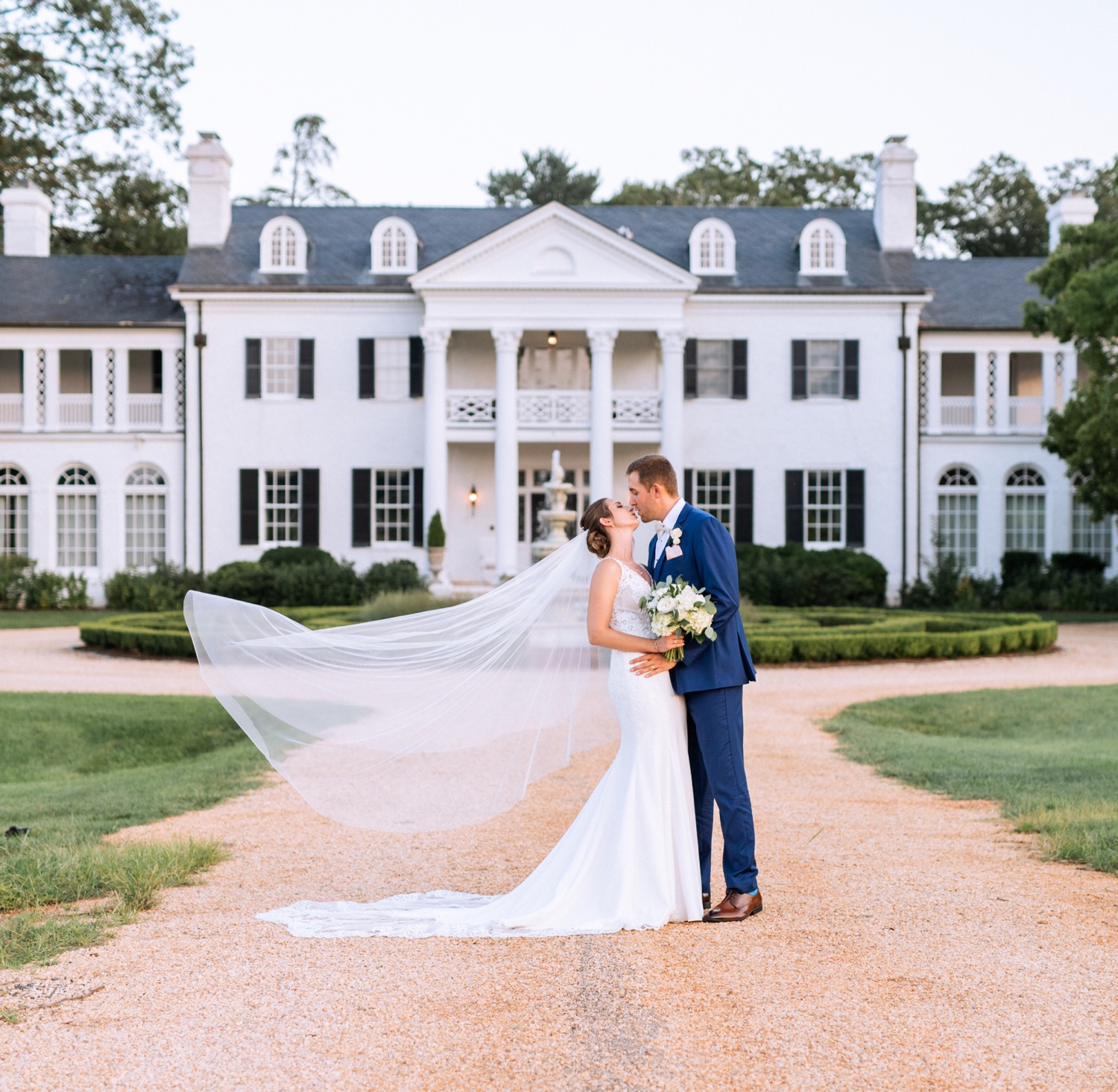 bride and groom kissing in front of the white mansion at keswick vineyards